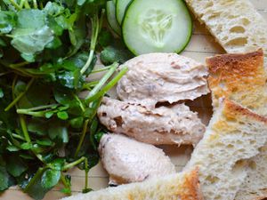 Closeup of several quenelles of gentleman's relish surrounded by toasts, cucumber slices, and watercress.