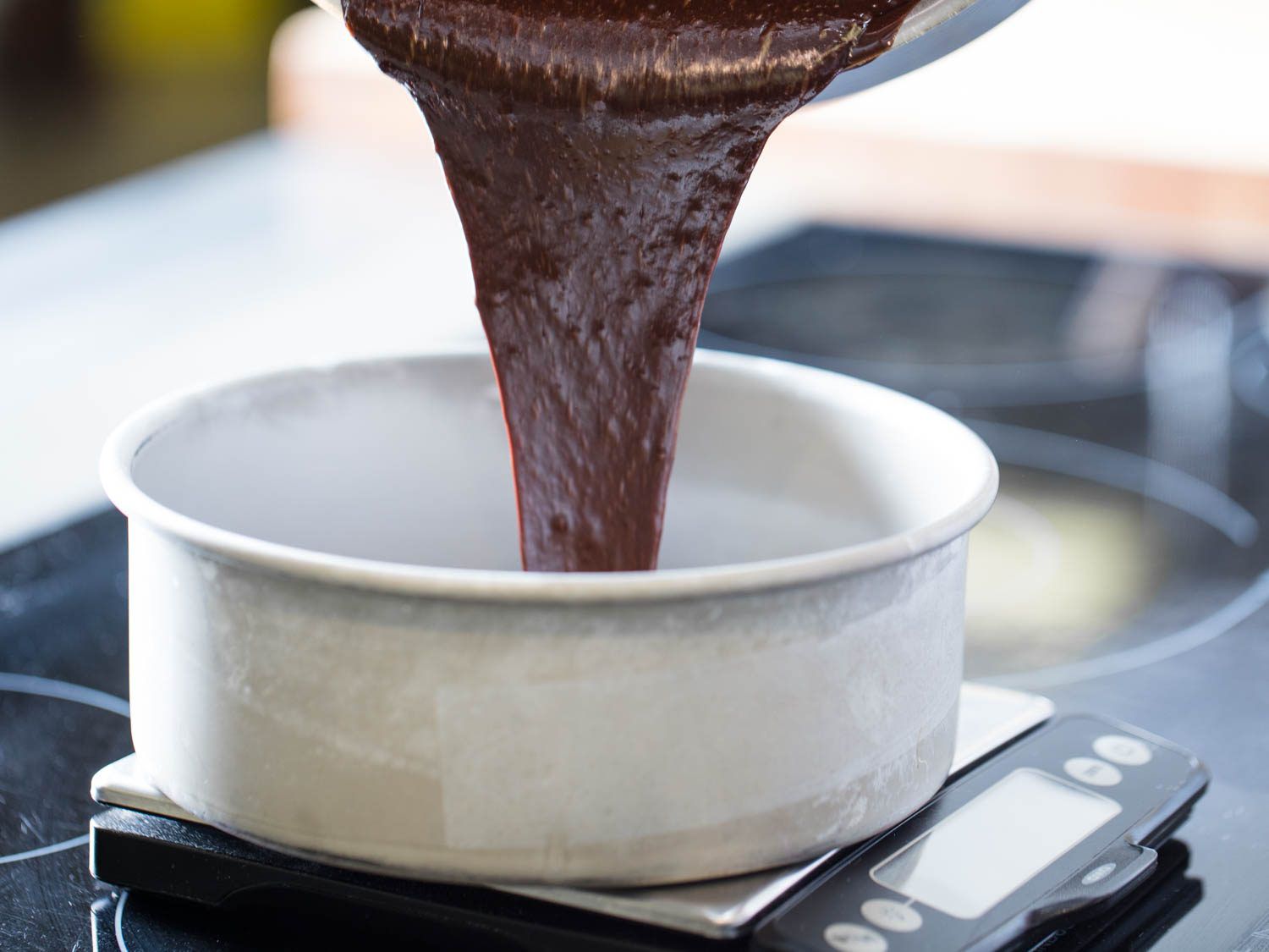 Pouring Devil's food cake batter into one 8-inch cake pan on a scale.