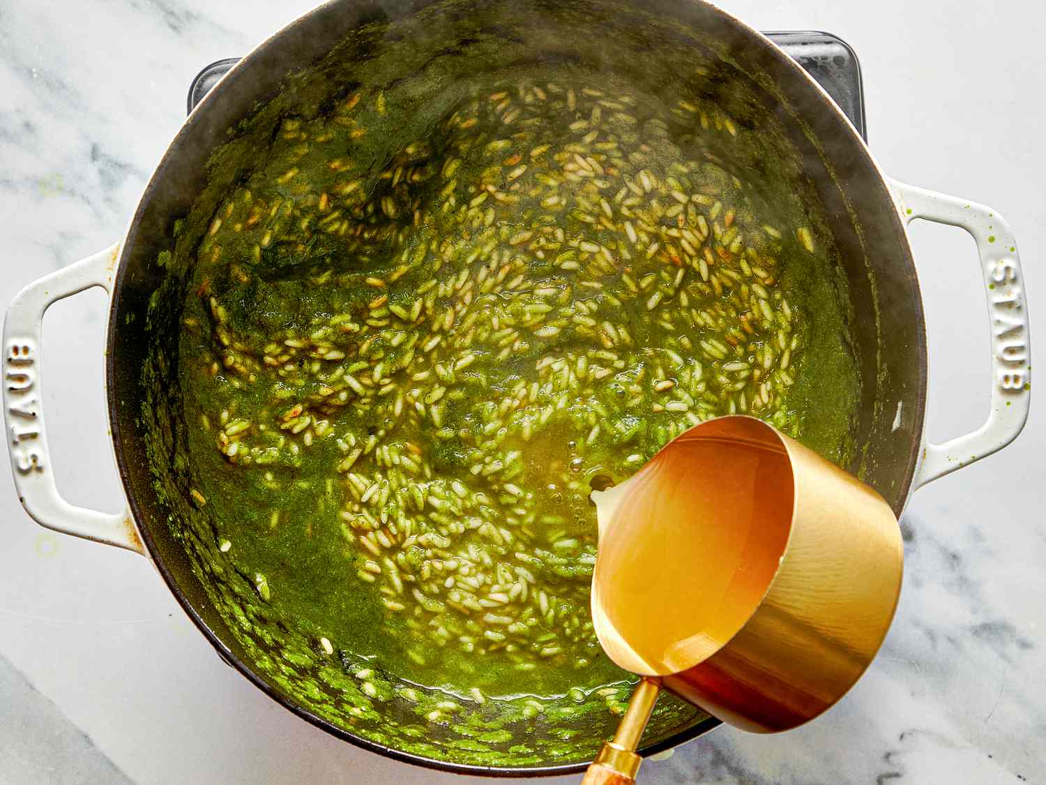 Cooking a pot of green rice with a brass measuring cup next to it viewed from above