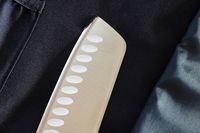 Closeup of a knife blade with a textured handle againstAsaya Chef Knife Roll Bag