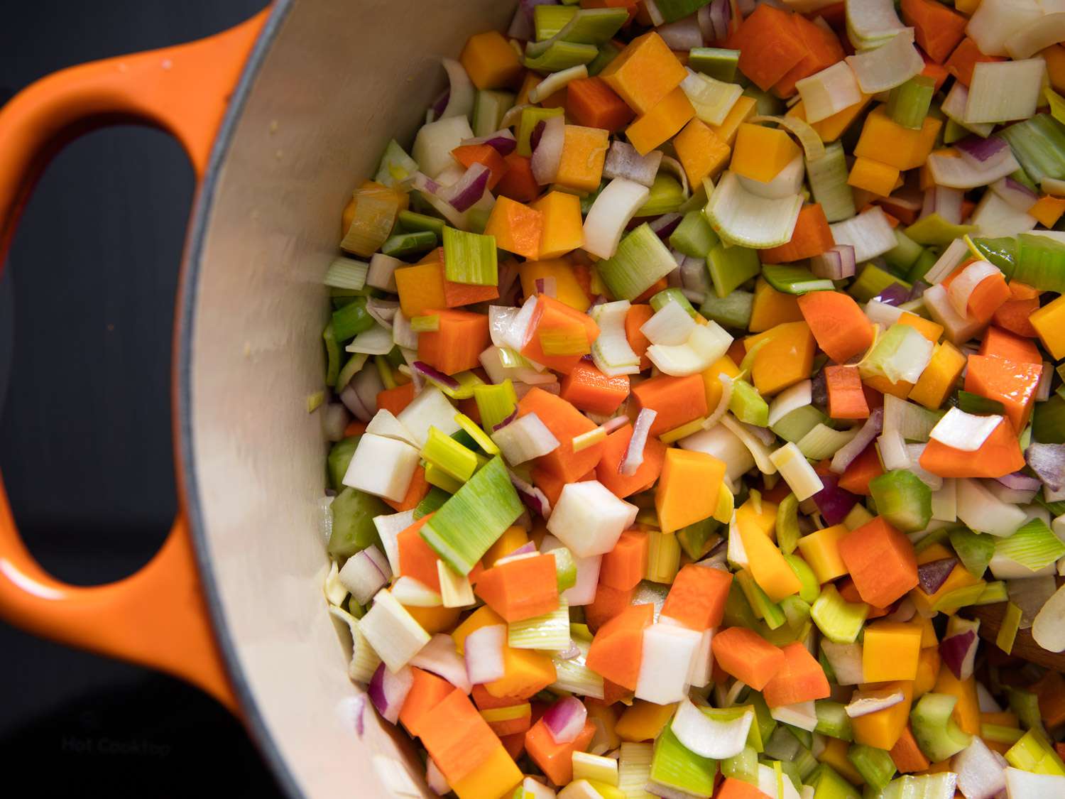Overhead closeup of diced onion, leek, carrots, squash, turnip, and celery cooking in a Dutch oven.