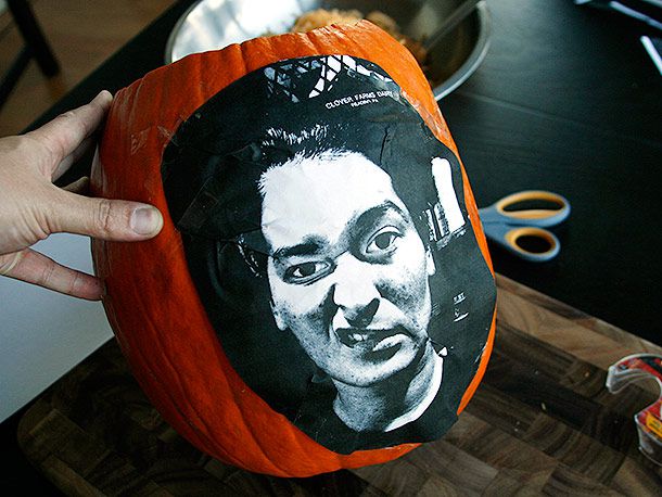 A pumpkin with a printed photo of a sneering woman's face taped to the outside