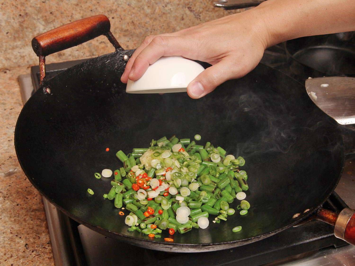 Sliced chiles, garlic, and scallions are added to the wok.