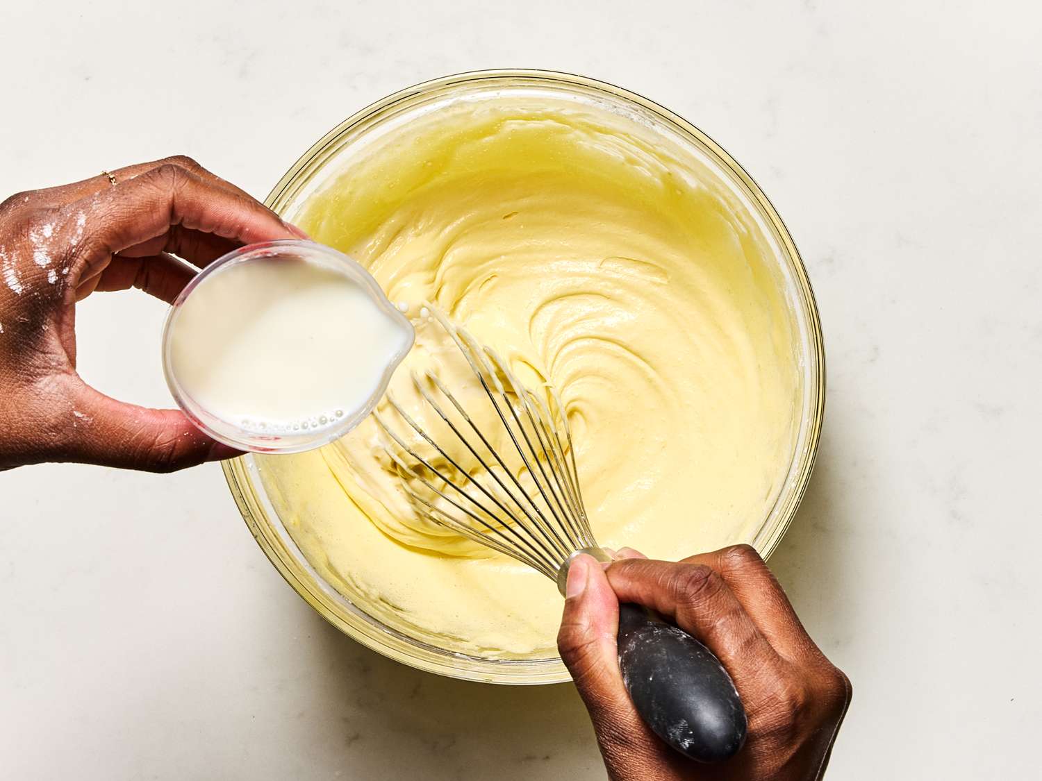 A person adds milk to a bowl of custard while whisking it