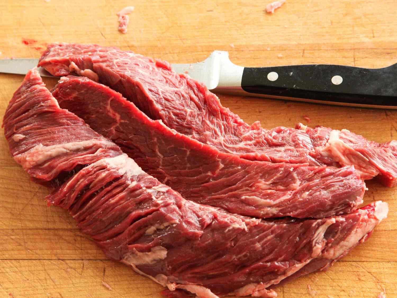 Three hanger steaks next to a knife on a wooden cutting board.
