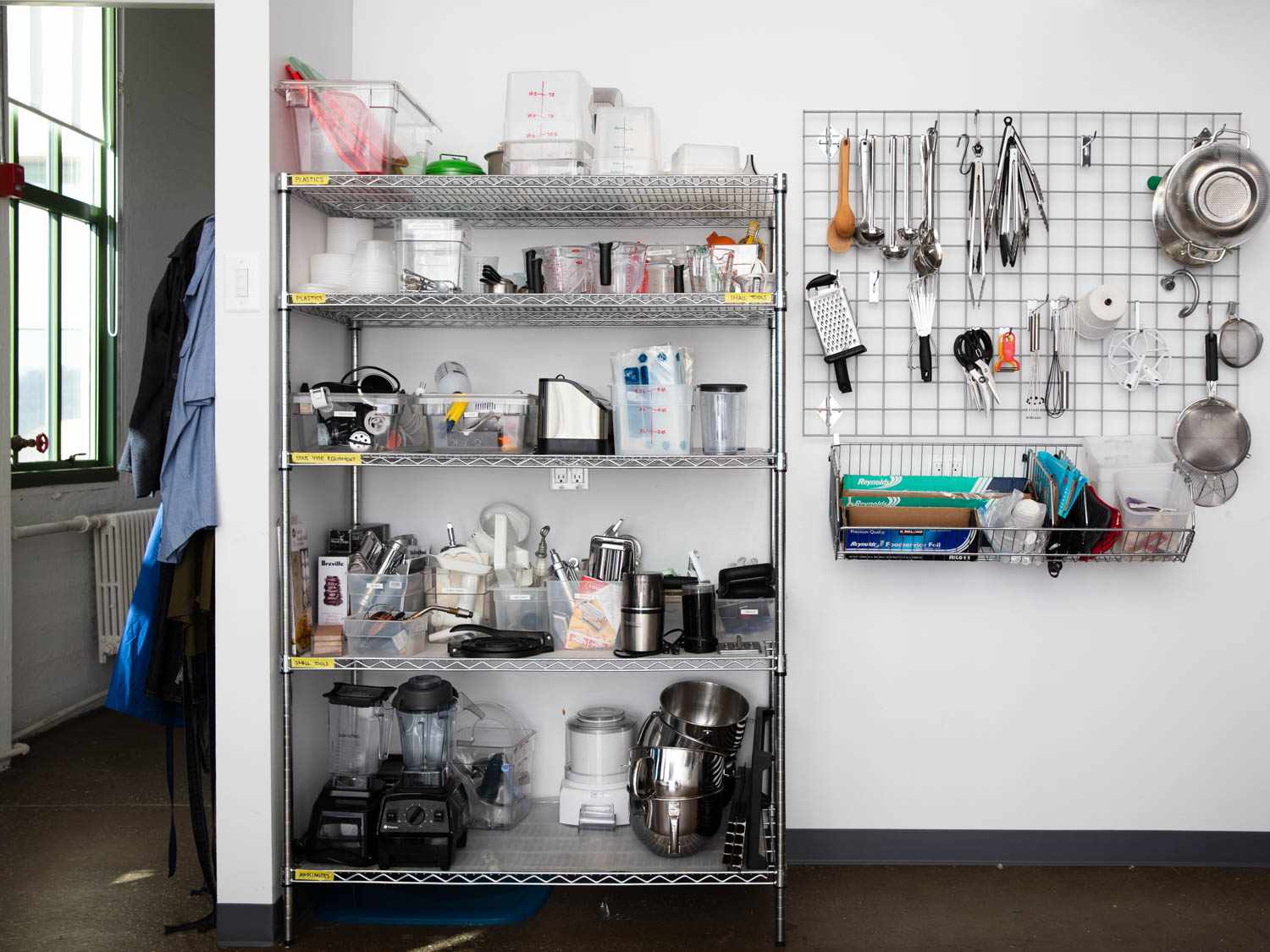 a wide shot of a metro rack shelving unit with kitchen equipment next to a wall-mounted wire grid for hanging kitchen tools
