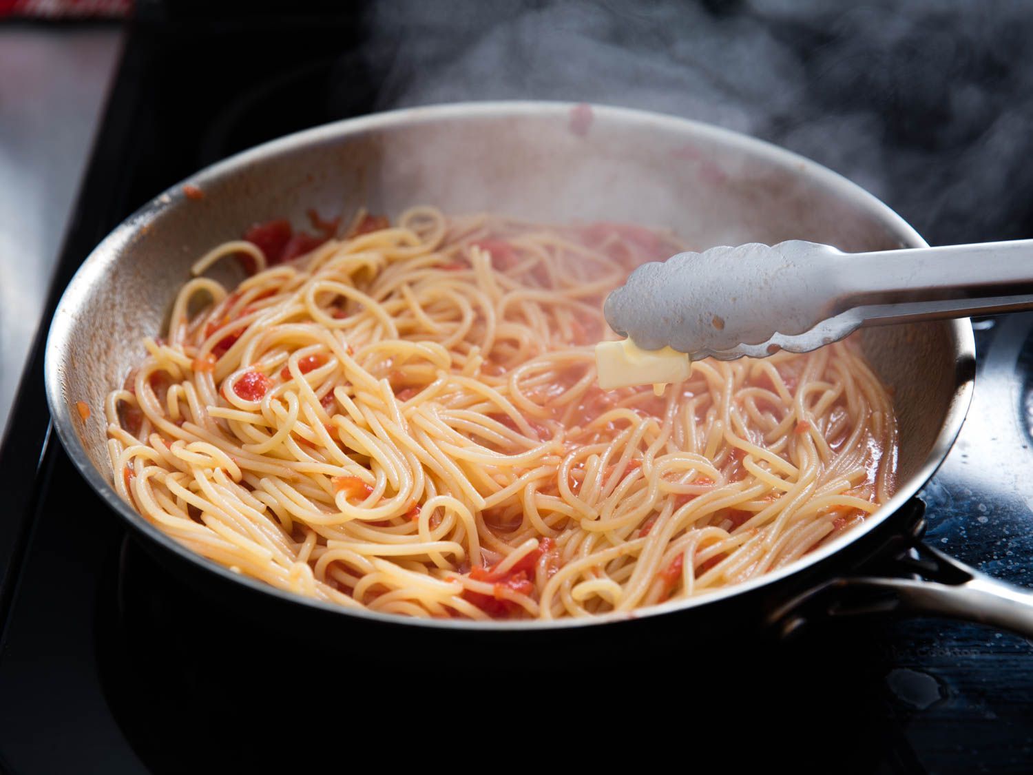 A cut of butter being added to the pasta and pasta sauce mixture.