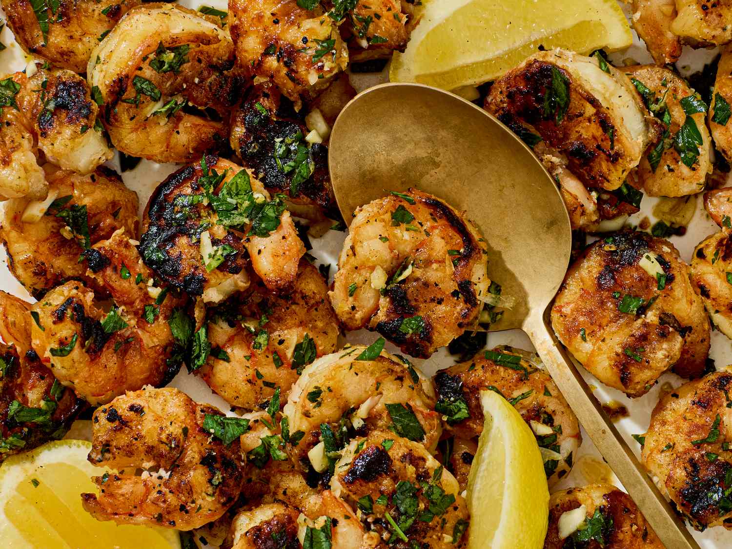 Grilled shrimp garnished with parsley and served with lemon wedges and a spoon