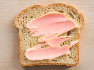 A slice of bread with pink spread on a light surface