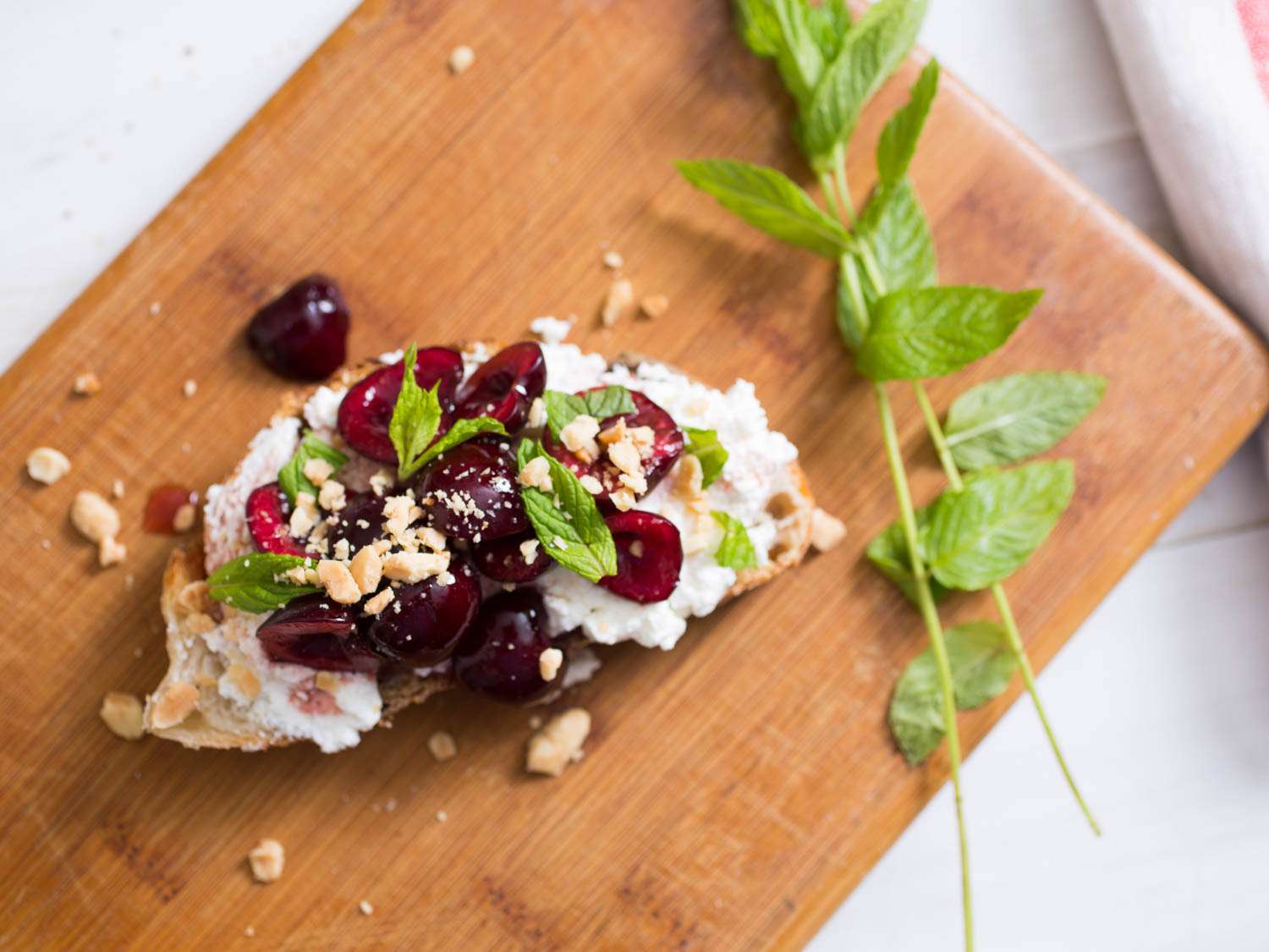 Overhead view of the ricotta, cherries, mint, and crushed almonds served on a slice of toast.