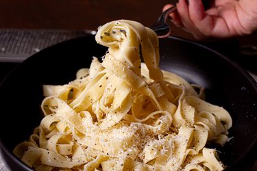 A plate of pasta being twirled on a fork topped with grated cheese and seasoning