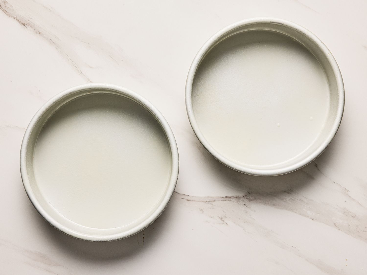 Two empty round baking pans on a marble countertop