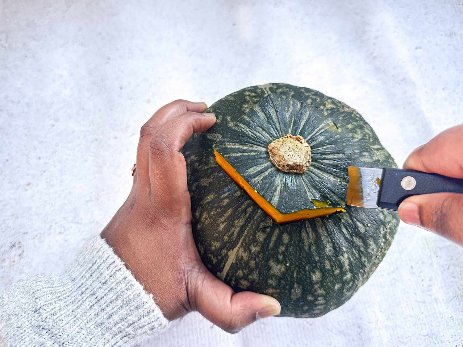 one hand holding a pumpkin, with the other hand cutting a pentagon shape into top of it with a knife 