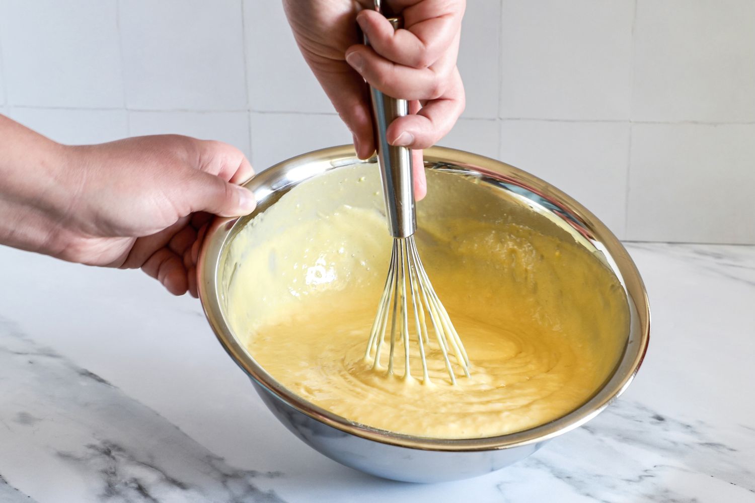 Hands whisking yellow batter in a Vollrath mixing bowl
