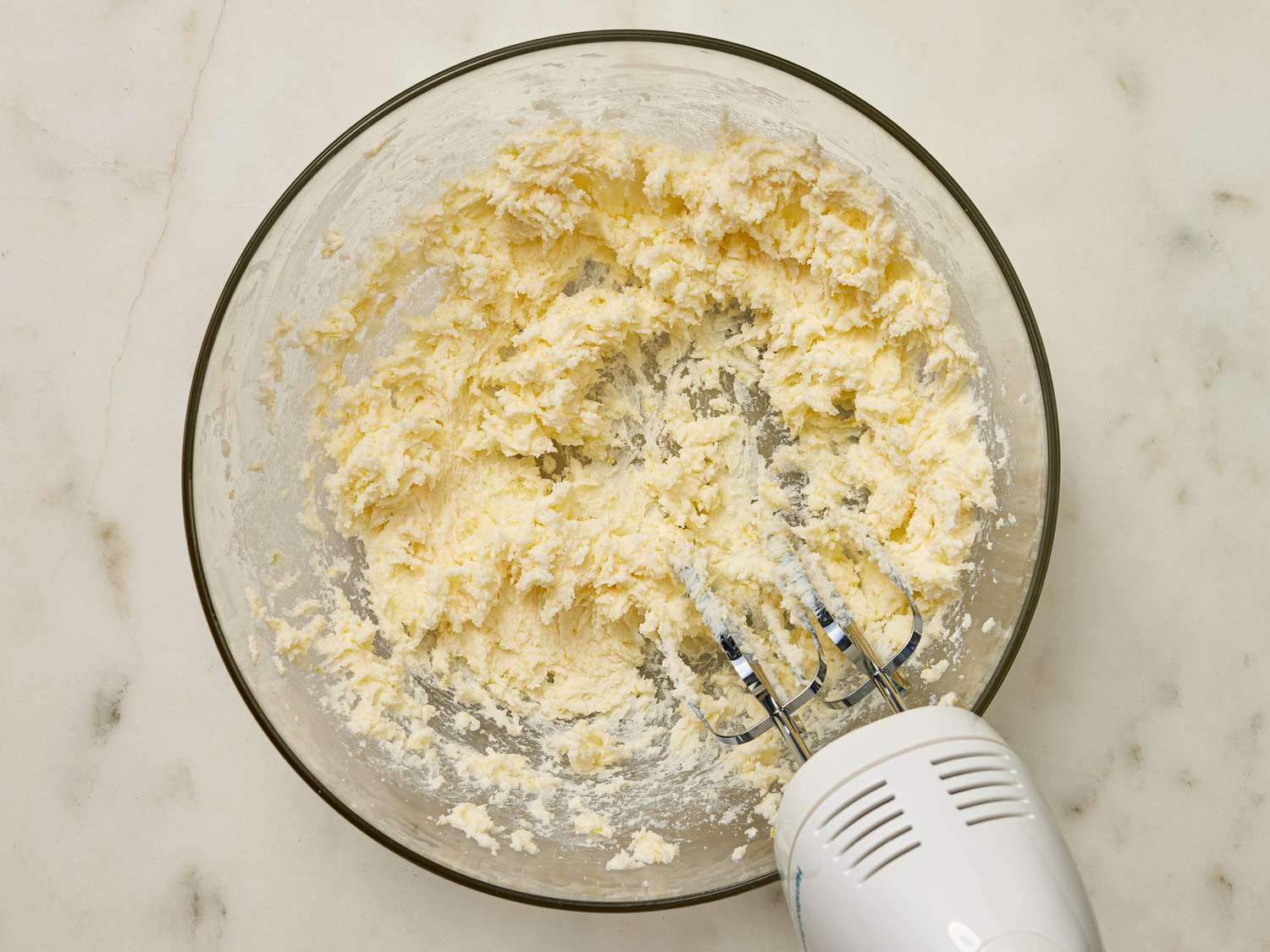 Electric mixer beating butter into sugar mixture in bowl