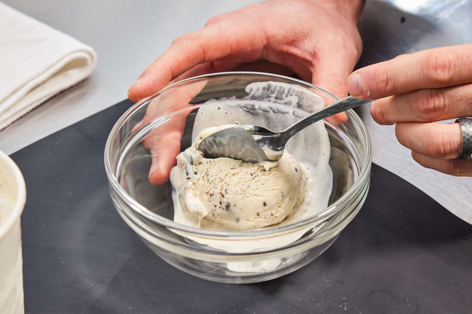 Person scooping ice cream from a glass bowl with a spoon on a table