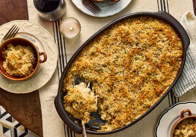 Large dish of French onion soup mac and cheese, with 2 cups of servings on dishes, a candle, a striped tablecloth