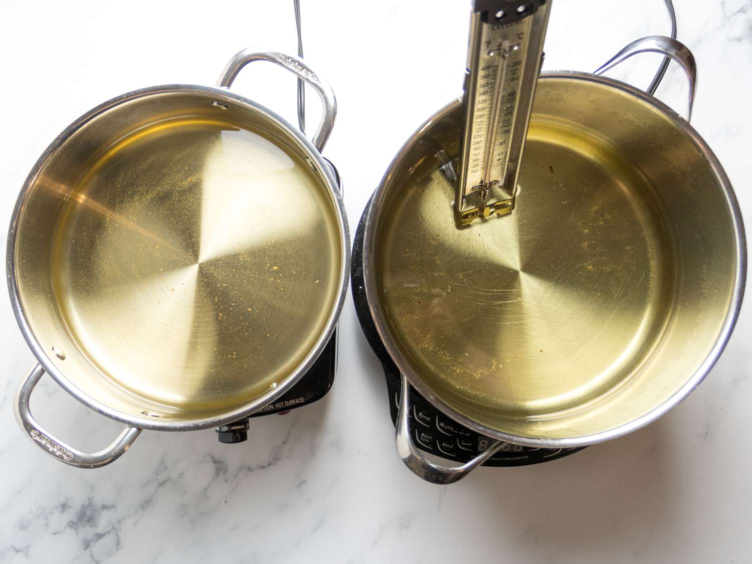 Two pots of hot oil, one with a thermometer inserted, on a stovetop