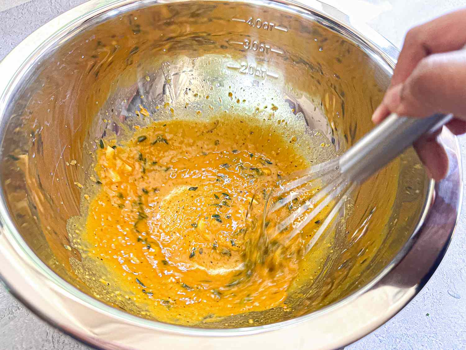 A hand whisking a mixture in a stainless steel bowl, ingredients being combined together