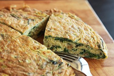 Clsoeup of a puffy ramp frittata, sliced into quarters on a cutting board.
