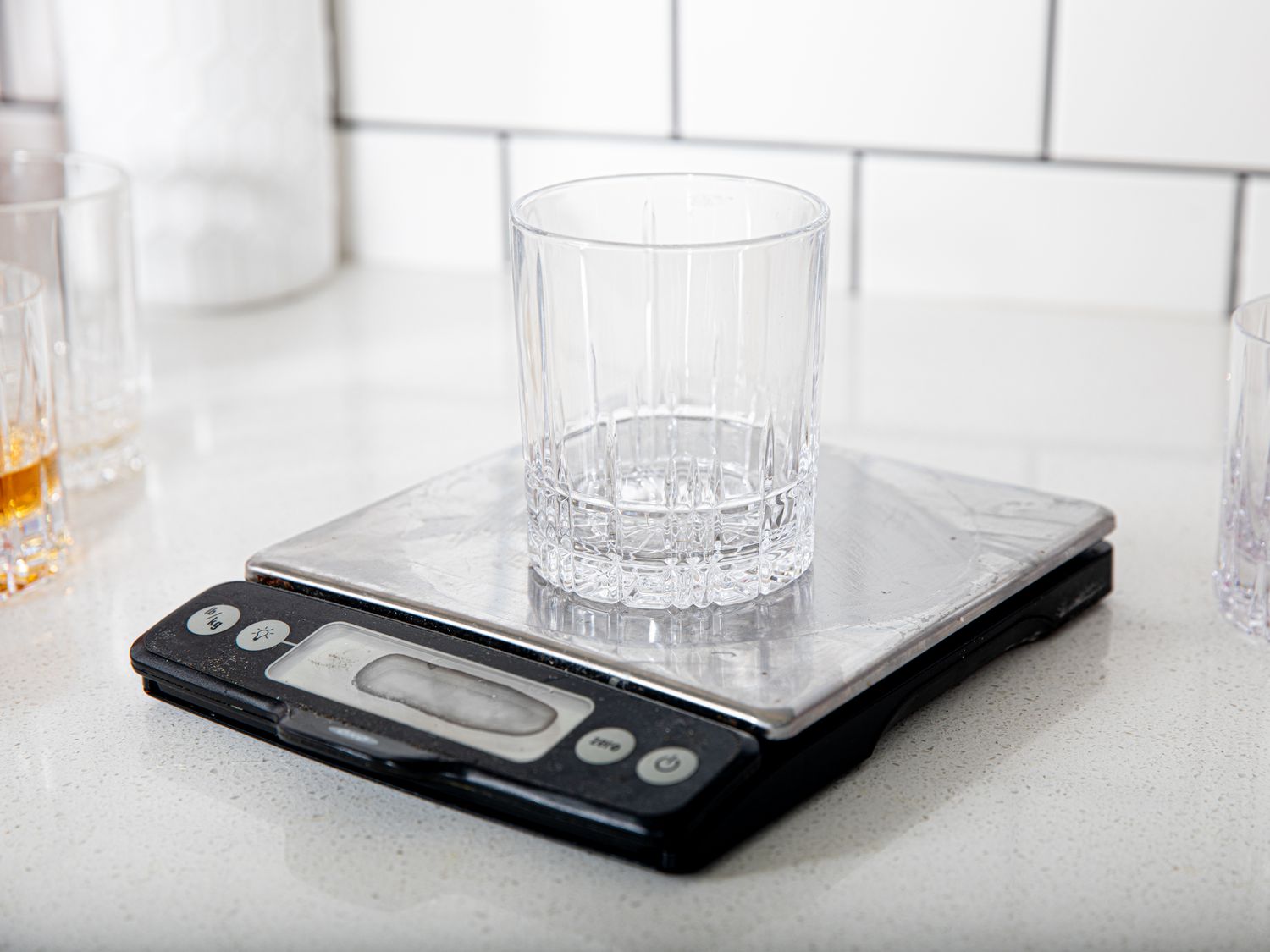 A rocks glass on a kitchen scale, with whiskey glasses in the background
