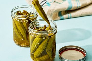 Two jars of pickled okra one jar with a fork lifting a piece of okra