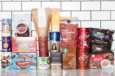 group of different hot chocolate packages stacked together on white surface with white tile background