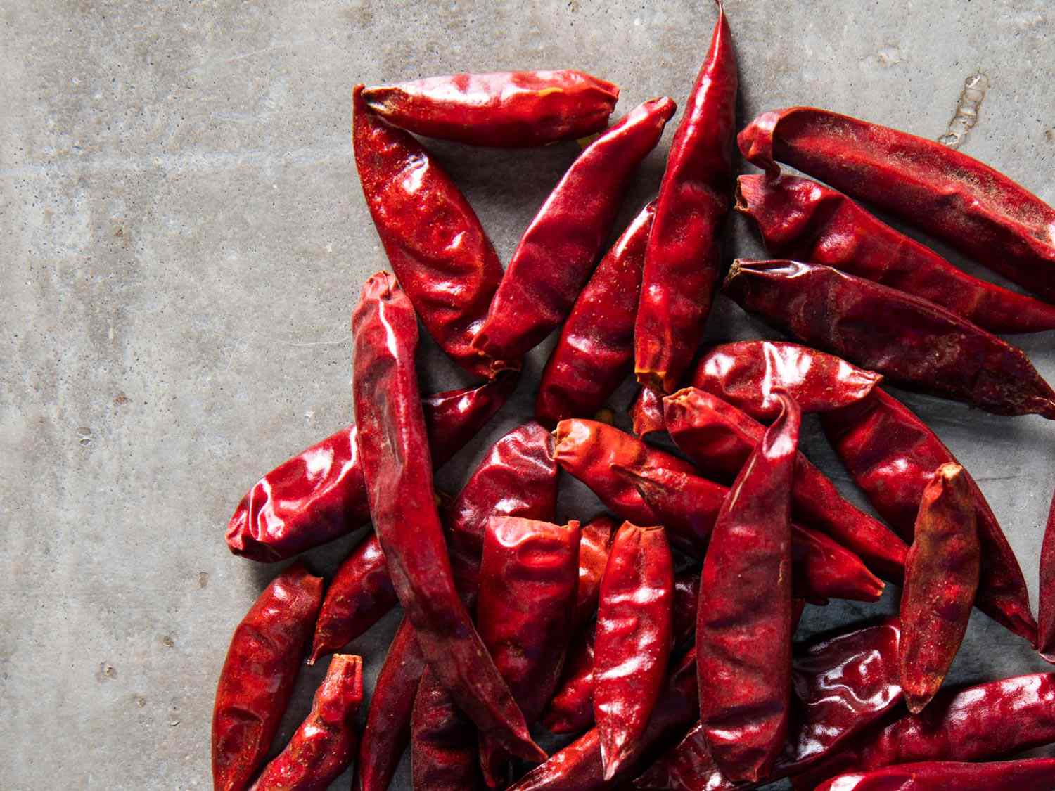 Overhead shot of bright red dried chilis on grey background