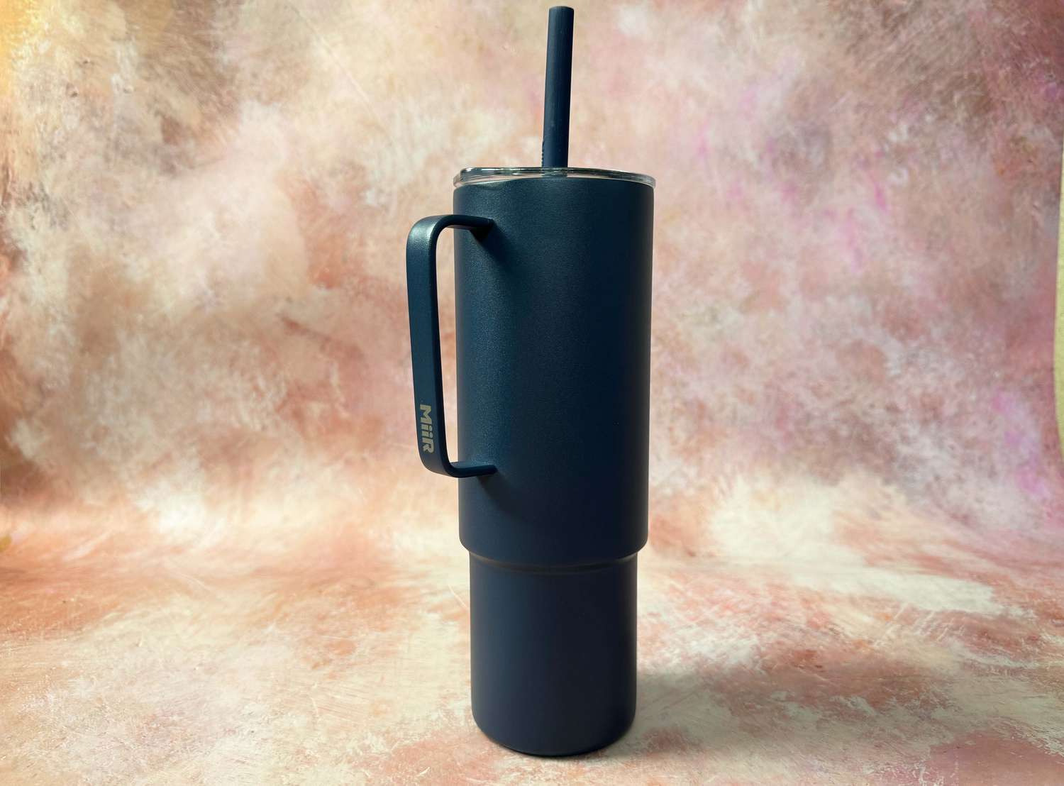 A dark blue MiiR insulated tumbler on a pink surface.