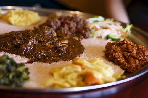 A large injera-lined platter topped with various Ethiopian dishes, many of which are flavored with niter kibbeh.