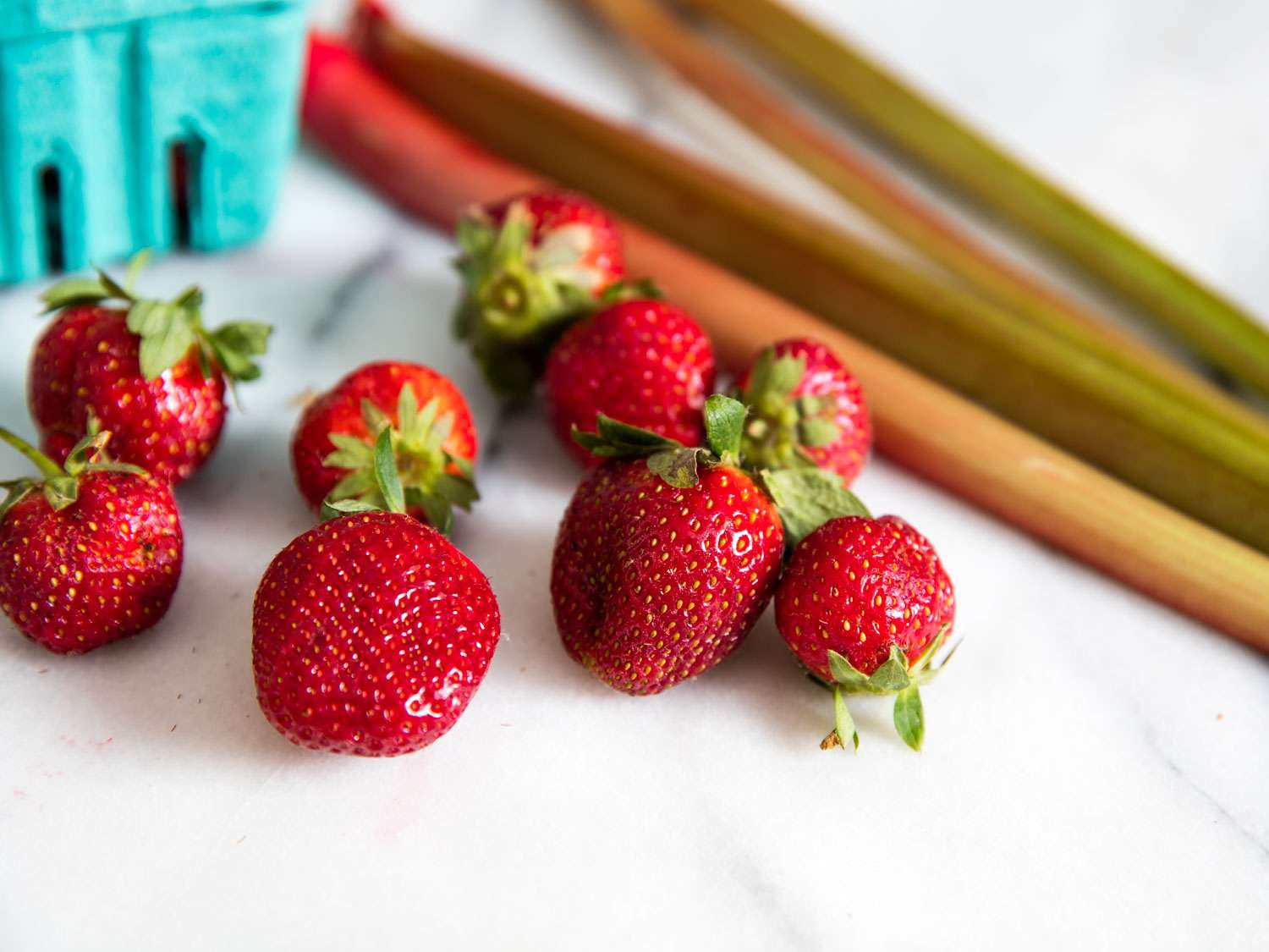 Whole strawberries and stalks of rhubarb on a marble counter.