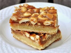 Closeup of two slices of salted cashew caramel bars, stacked together on a small white plate.