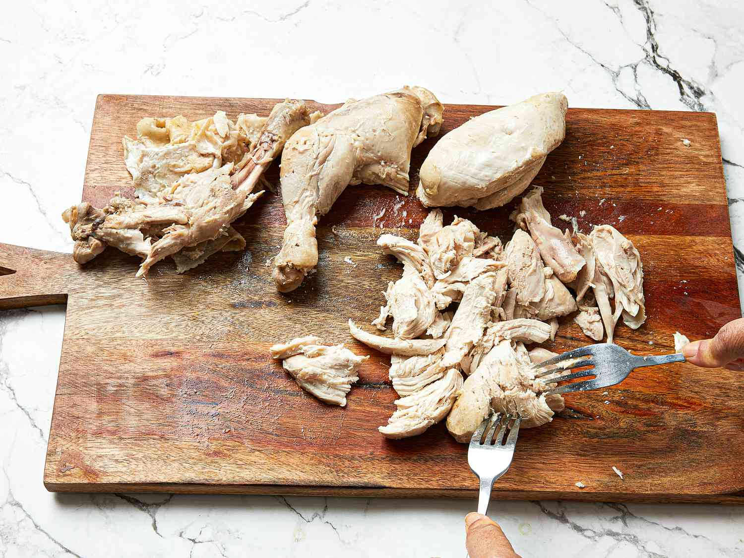 Shredding chicken with 2 large forks on a cutting board 