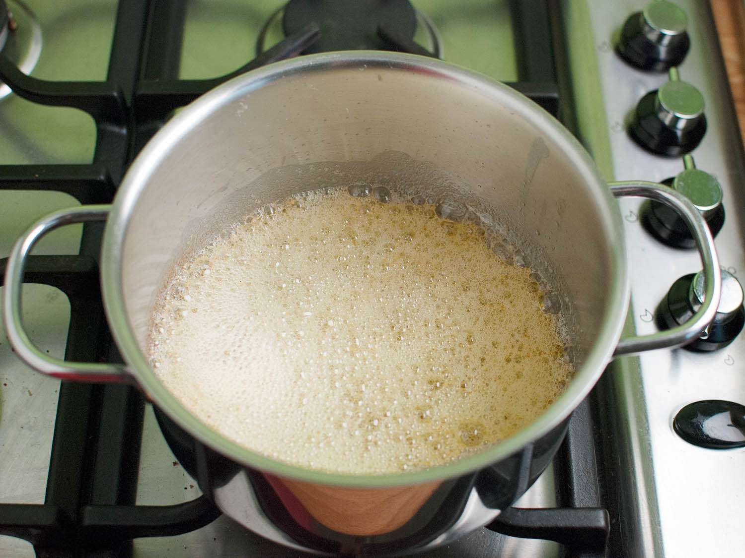 A metal pot of melted butter with the top of the butter covered in a layer of foam.