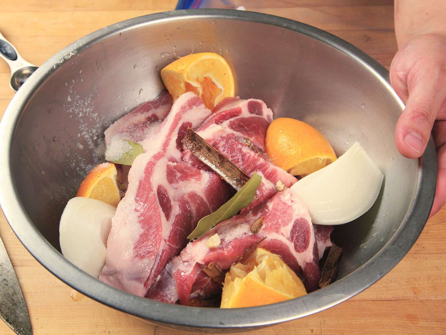 Pork marinating with quartered onions, garlic, cinnamon, bay leaves, and quartered oranges.
