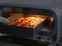 a person removing a pan pizza from an indoor pizza oven