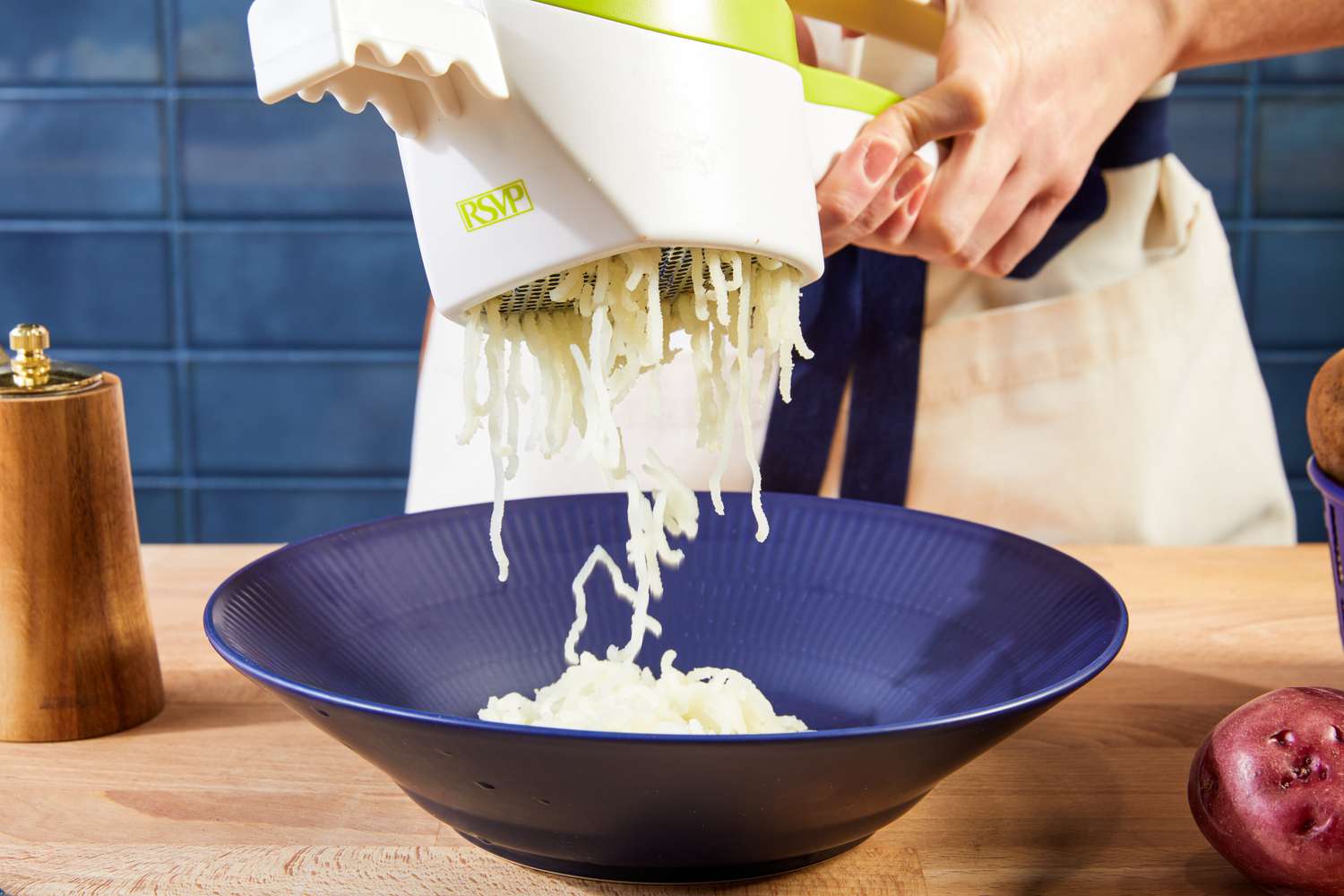A person using a potato ricer to rice potatoes into a blue bowl.