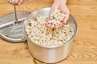 A person grabs a handful of popcorn from a Wabash Valley Farms Original Whirley Pop.