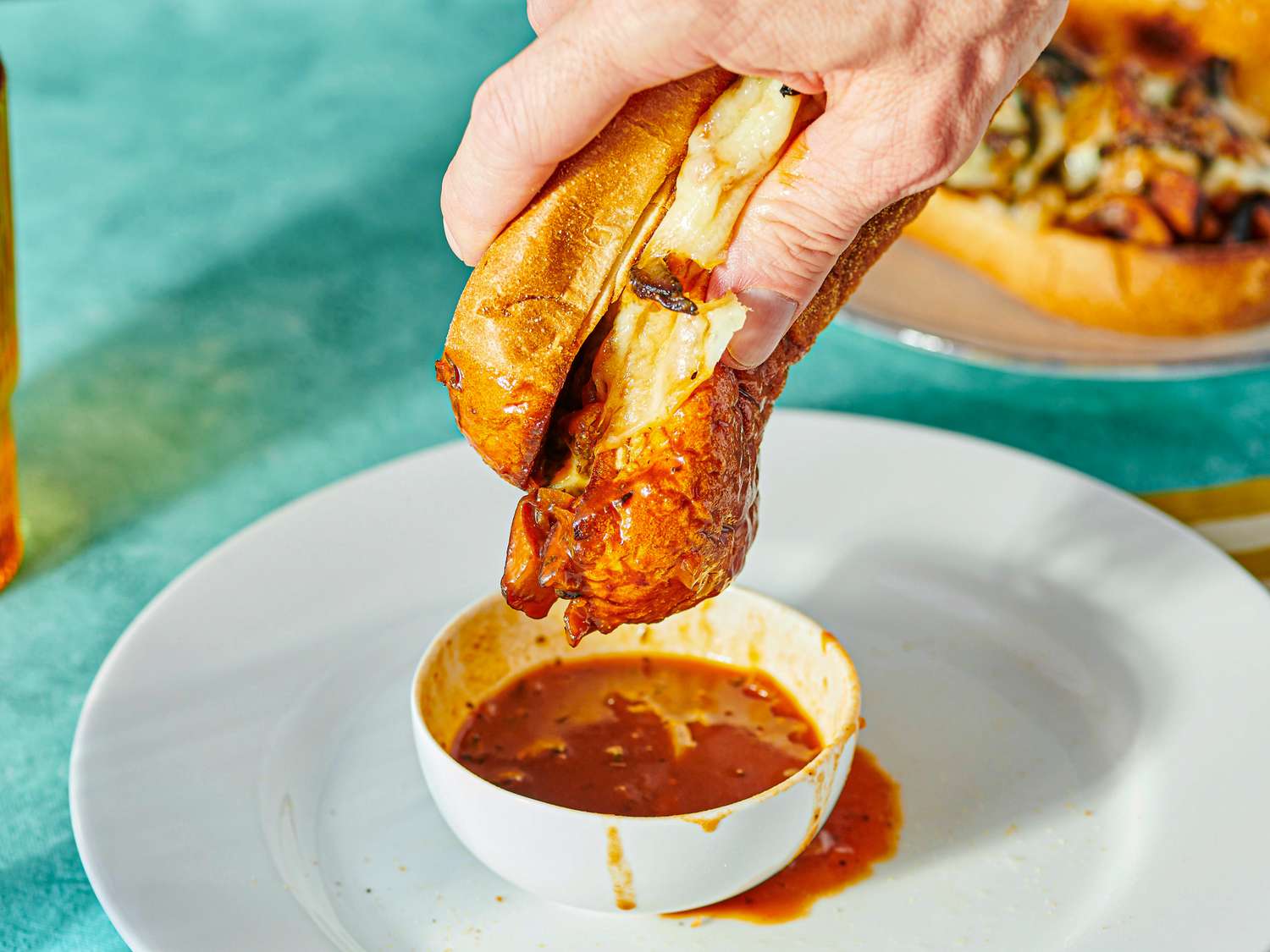 A hand dipping a sandwich into a bowl of sauce on a plate