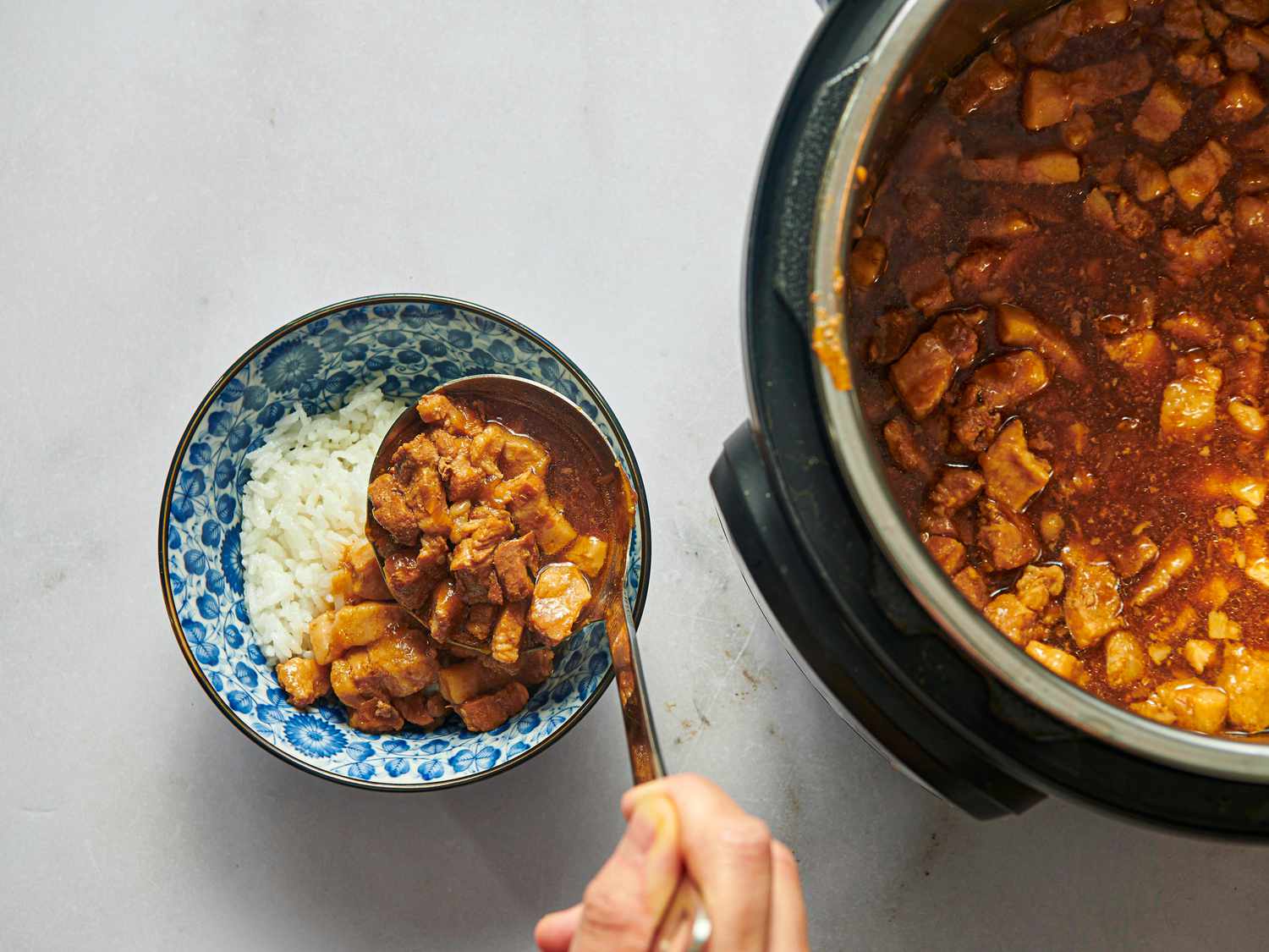 spooning braised minced pork onto white rice in a blue bowl. 