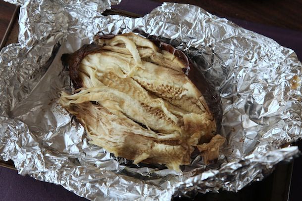 A whole roasted eggplant, cradled in the foil it was roasted in. Some of the skin has been removed and the flesh has prodded apart.