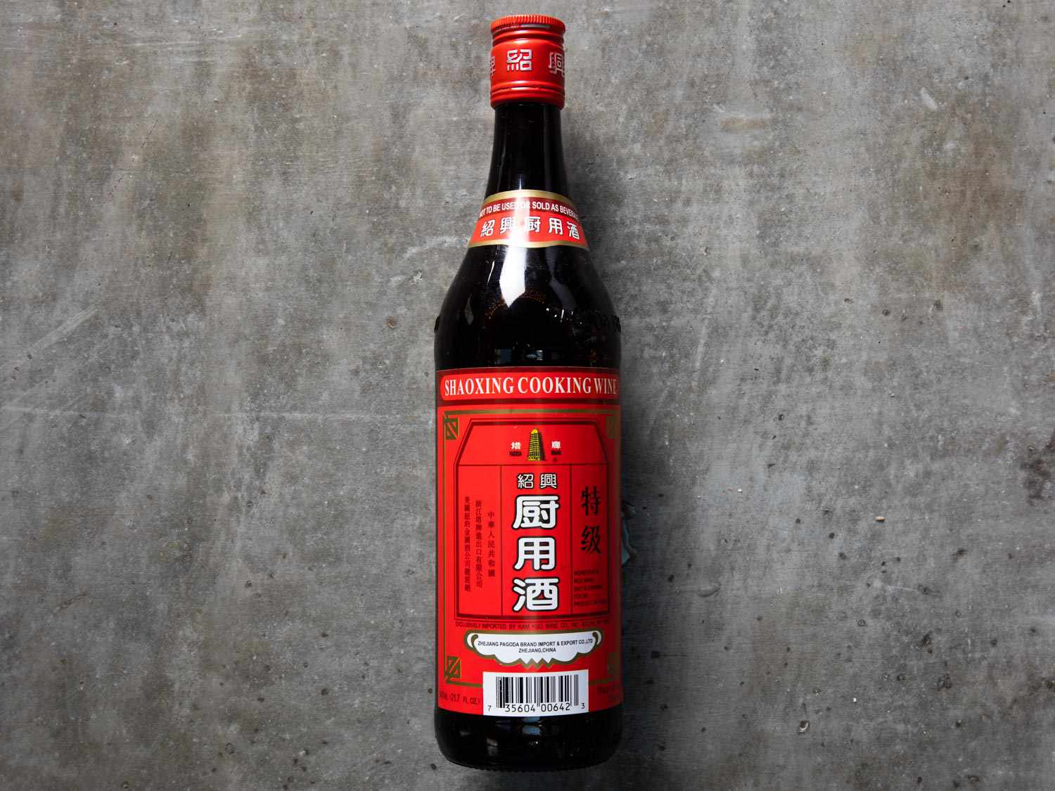 Bottle of black Shaoxing wine with red label against grey background