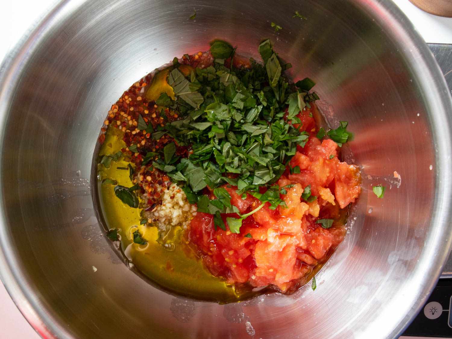 A mixing bowl containing grated tomatoes, parsley, chile flakes, and olive oil.