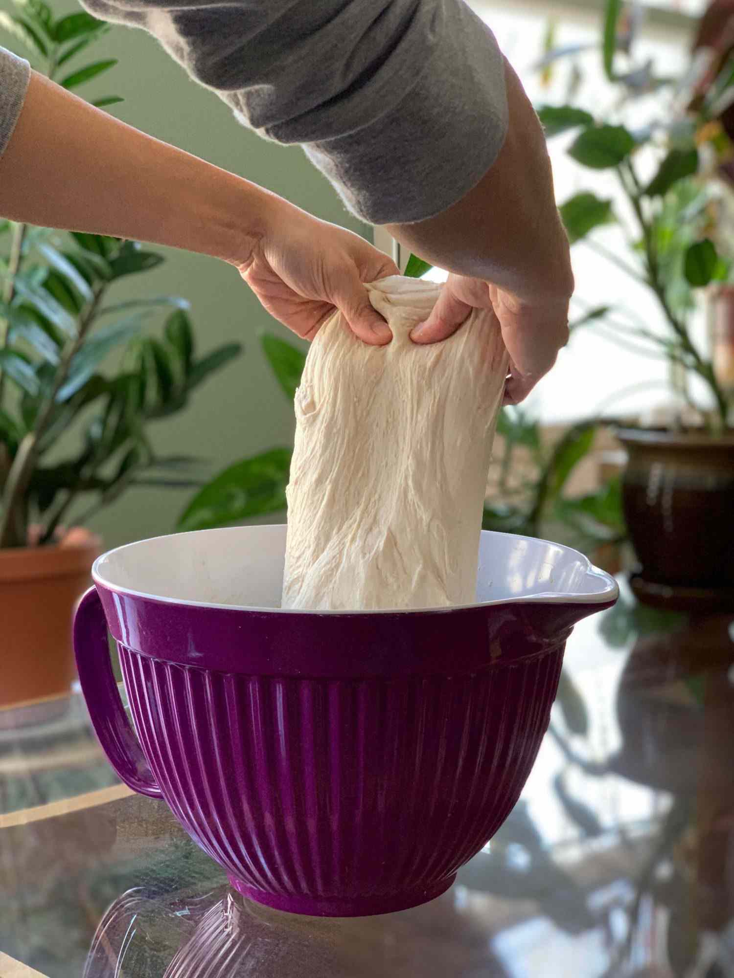 Hands lifting up sourdough bread dough