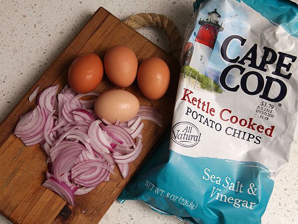 Overhead view of a bag of salt-and-vinegar chips, 4 eggs, and a pile of sliced red onion.