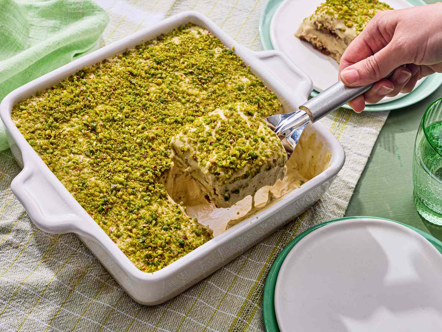 A square dessert dish of pistachio tiramisu with a portion being served
