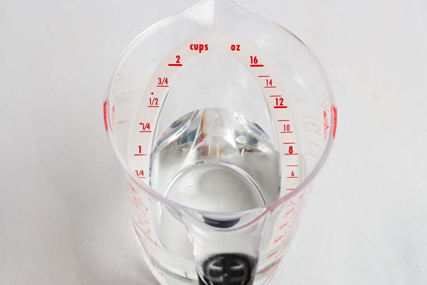An OXO plastic measuring cup with a liquid and marked in cups and ounces