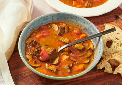 Kansas City Steak soup in bowl on wooden board with spoonful of soup, bread, and another bowl in thebackground