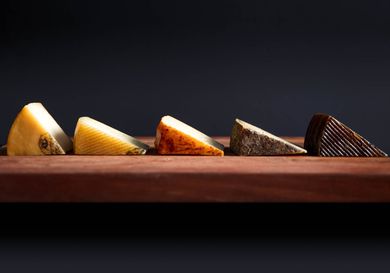 Profile view of five different Manchego-type cheeses, cut into wedges and arranged on a wooden board.