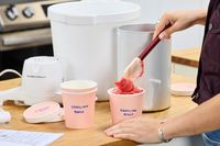 A person using a spatula to move ice cream from the Hamilton Beach Automatic Ice Cream Maker into a pint